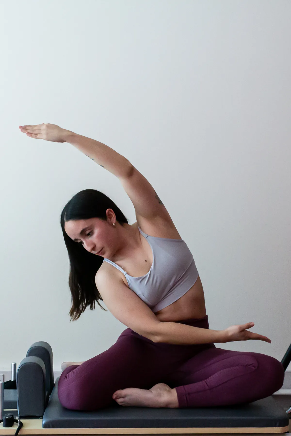 Mujer sentada en el reformer en un estiramiento lateral, con la mirada hacia abajo.